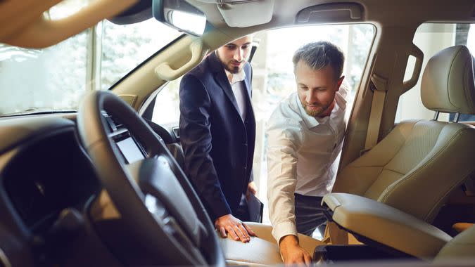 Professional salesmen selling cars at dealership to buyer.