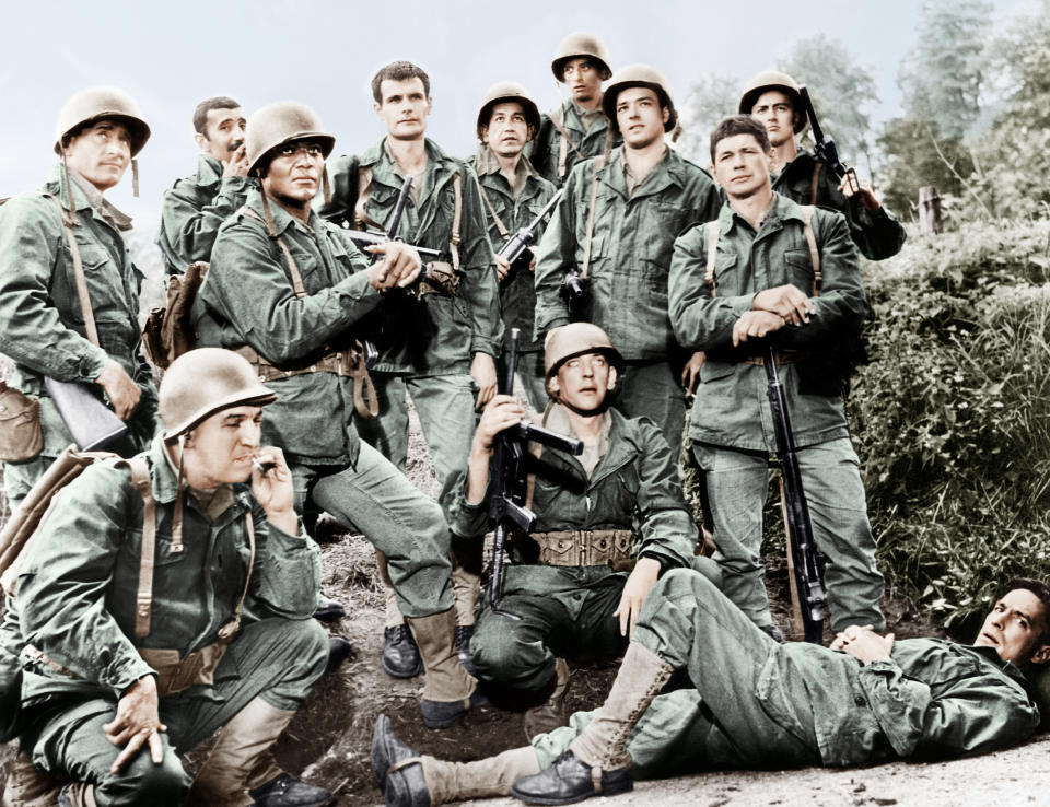 Cast members of the film "The Dirty Dozen" wearing military uniforms and helmets, posing together outdoors