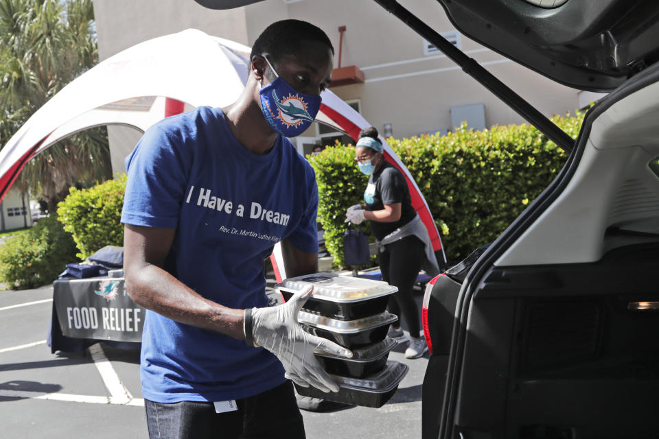 David Moimeme loads prepared meals into a vehicle as United Way of Broward County partners with the Miami Dolphins football team to distribute backpacks and meals to military families in need during the coronavirus pandemic, Wednesday, Aug. 5, 2020, in Fort Lauderdale, Fla. (AP Photo/Lynne Sladky)