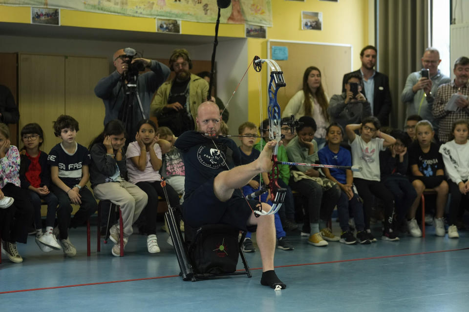 Archer Matt Stutzman of United States holds the bow with his foot during a performance in a Paris school, in Paris, Wednesday, Oct. 4, 2023. Visiting France's capital before Paralympic tickets go on sale next week, Stutzman dropped by a Paris school on Wednesday and wowed its young pupils with his shooting skills. (AP Photo/Thibault Camus)