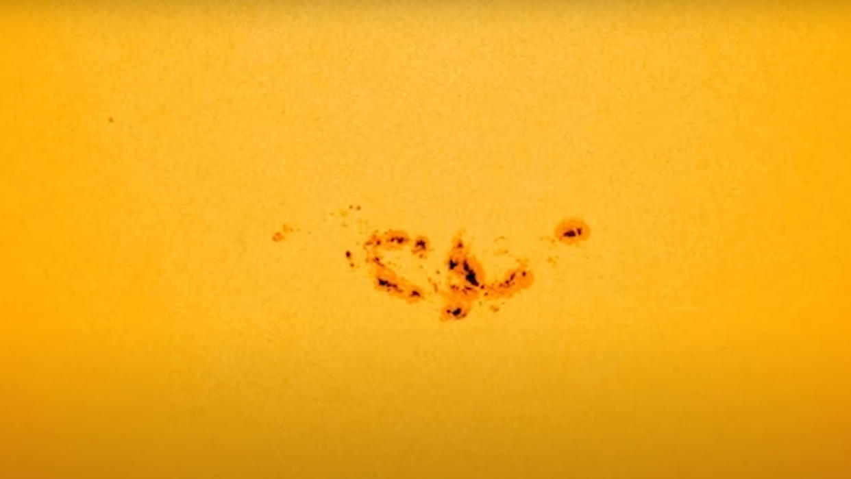  Spacecraft view of a patch of the sun's yellow surface, showing a large, dark, irregular sunspot. 