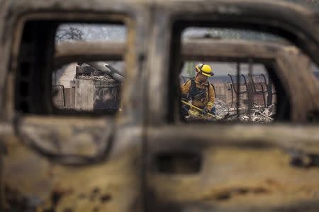 A firefighter is seen through destroyed cars as he searches for victims in the rubble of a home burnt by the Valley Fire in Middletown, California, September 14, 2015. REUTERS/David Ryder