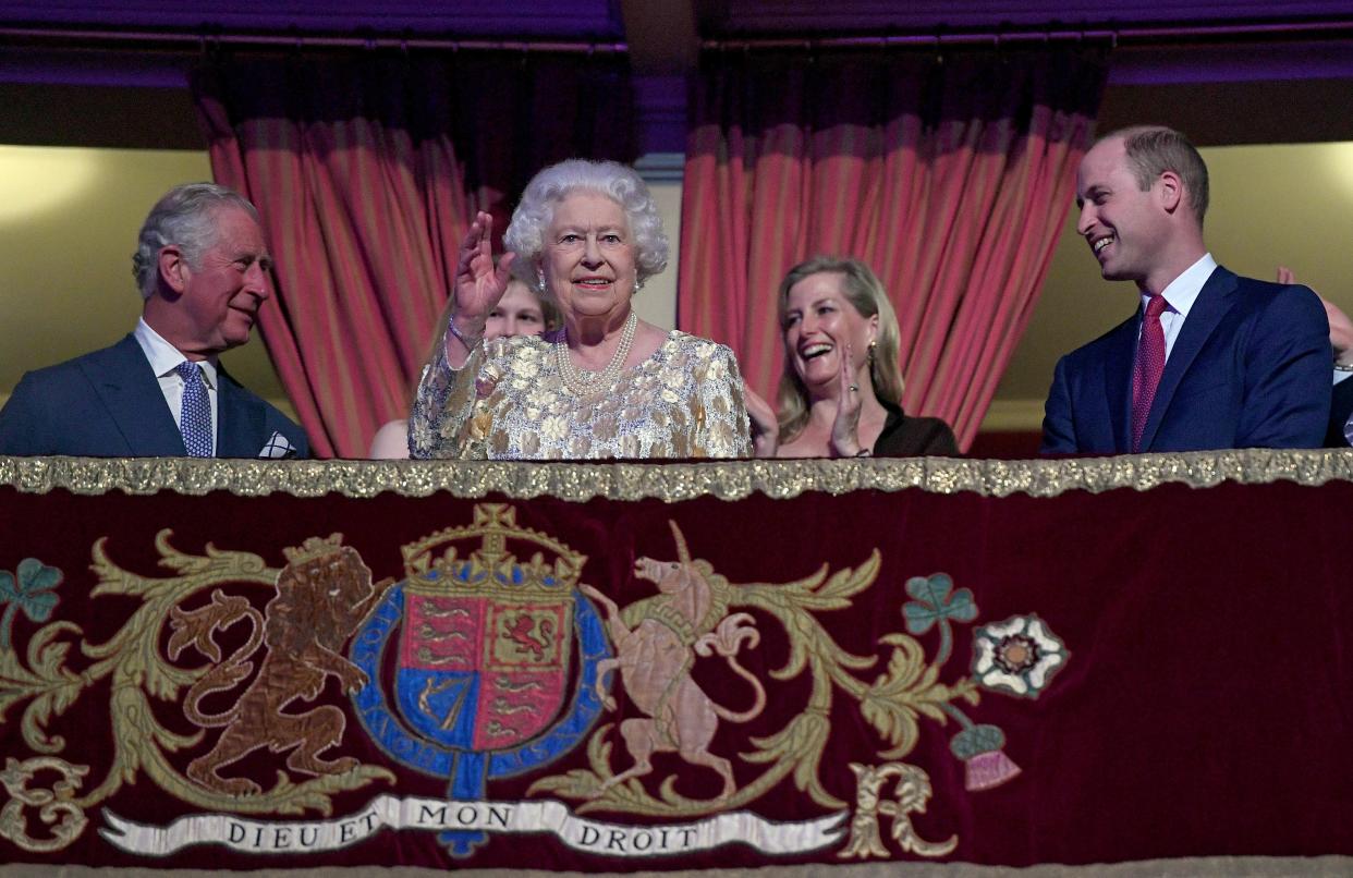 TOPSHOT - Britain's Queen Elizabeth II (centre L) waves to guests as her son Britain's Prince Charles, Prince of Wales (L) and grandson Britain's Prince William, Duke of Cambridge (R) react as she takes her seat ni the Royal box during The Queen's Birthday Party concert on the occassion of Her Majesty's 92nd birthday at the Royal Albert Hall in London on April 21, 2018. (Photo by Andrew Parsons / POOL / AFP) (Photo by ANDREW PARSONS/POOL/AFP via Getty Images)