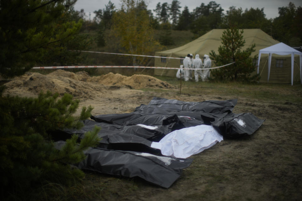 Plastic bags with bodies inside lie on the ground as members of a forensic team work at an exhumation in a mass grave in Lyman, Ukraine, Tuesday, Oct. 11, 2022. (AP Photo/Francisco Seco)