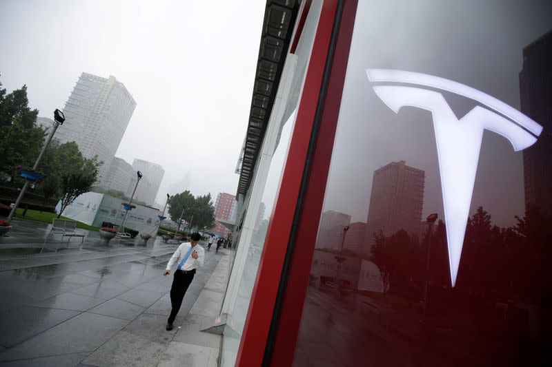 FILE PHOTO: A man walks near a logo of Tesla outside its China headquarters at China Central Mall in Beijing, China July 11, 2018. REUTERS/Jason Lee/File Photo