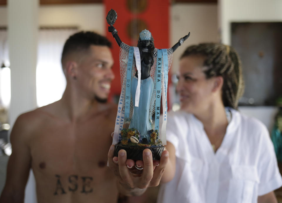 Brazilian soccer star Paulinho and his mother Ana Christina Sampaio pose for a photo with a small statue of the sea goddess Yemanja, at their home in Belo Horizonte, Brazil, Sunday, Sept. 17, 2023. Growing up in Rio de Janeiro, Paulinho said he suffered prejudice because of his Candomble faith, like his mother and grandmother before him. (AP Photos/Thomas Santos)