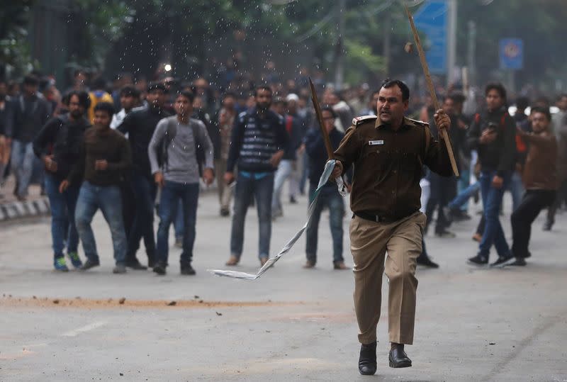 A police officer runs for cover during a protest against the Citizenship Amendment Bill in New Delhi