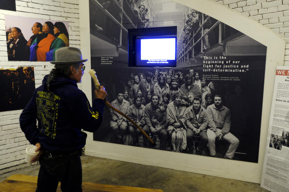 In this photo taken Tuesday, Nov. 12, 2019, Eloy Martinez, who took part in the Native American occupation of Alcatraz 50 years earlier, looks over a group photograph showing the occupiers displayed in an exhibit on the island in San Francisco. The week of Nov. 18, 2019, marks 50 years since the beginning of a months-long Native American occupation at Alcatraz Island in the San Francisco Bay. The demonstration by dozens of tribal members had lasting effects for tribes, raising awareness of life on and off reservations, galvanizing activists and spurring a shift in federal policy toward self-determination. (AP Photo/Eric Risberg)