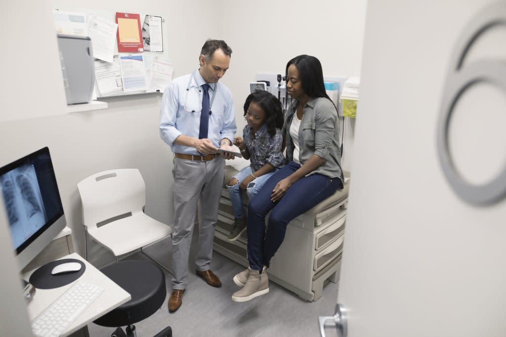 a physician talks to a moth and daughter in an examination room