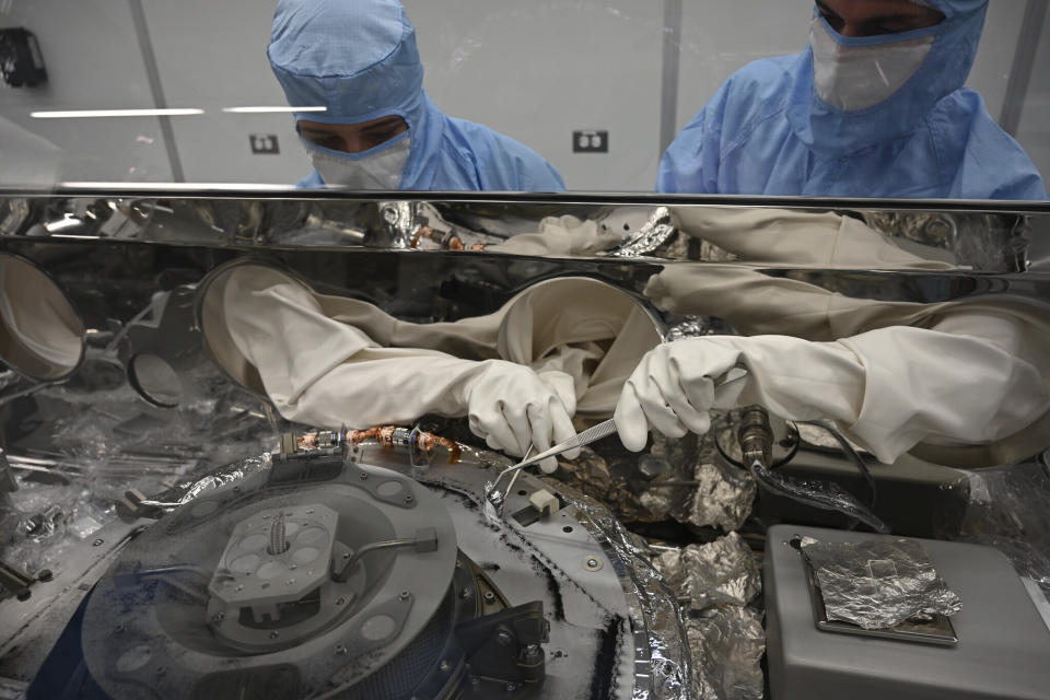 ARCHIVO - En esta fotografía proporcionada por la NASA se ve a Mari Montoya (izquierda) y a Curtis Calva mientras utilizan herramientas para recolectar partículas de un asteroide en la base de un contenedor, el 27 de septiembre de 2023, en el Centro Espacial Johnson, en Houston. (NASA vía AP, Archivo)