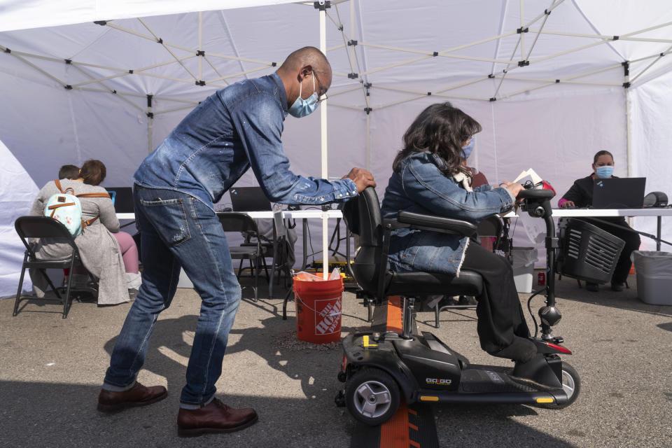 Veronica Lopez, who has Spina bifida, is helped by a staff member of the St. John's Well Child and Family Center's COVID-19 vaccination site before getting her vaccine at the East Los Angeles Civic Center in Los Angeles, Thursday, March 4, 2021. California will begin setting aside 40% of all vaccine doses for the state's most vulnerable neighborhoods in an effort to inoculate people most at risk from the coronavirus more quickly. (AP Photo/Damian Dovarganes)