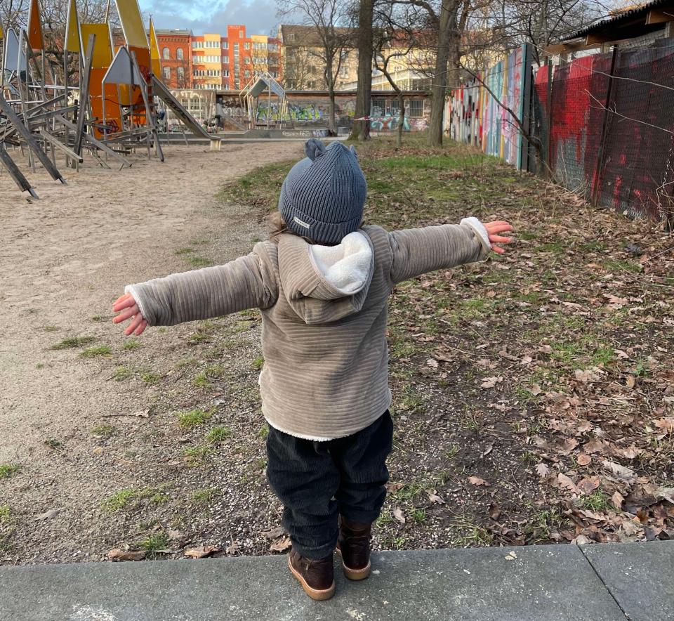 Toddler standing near playground with his hands out in the air