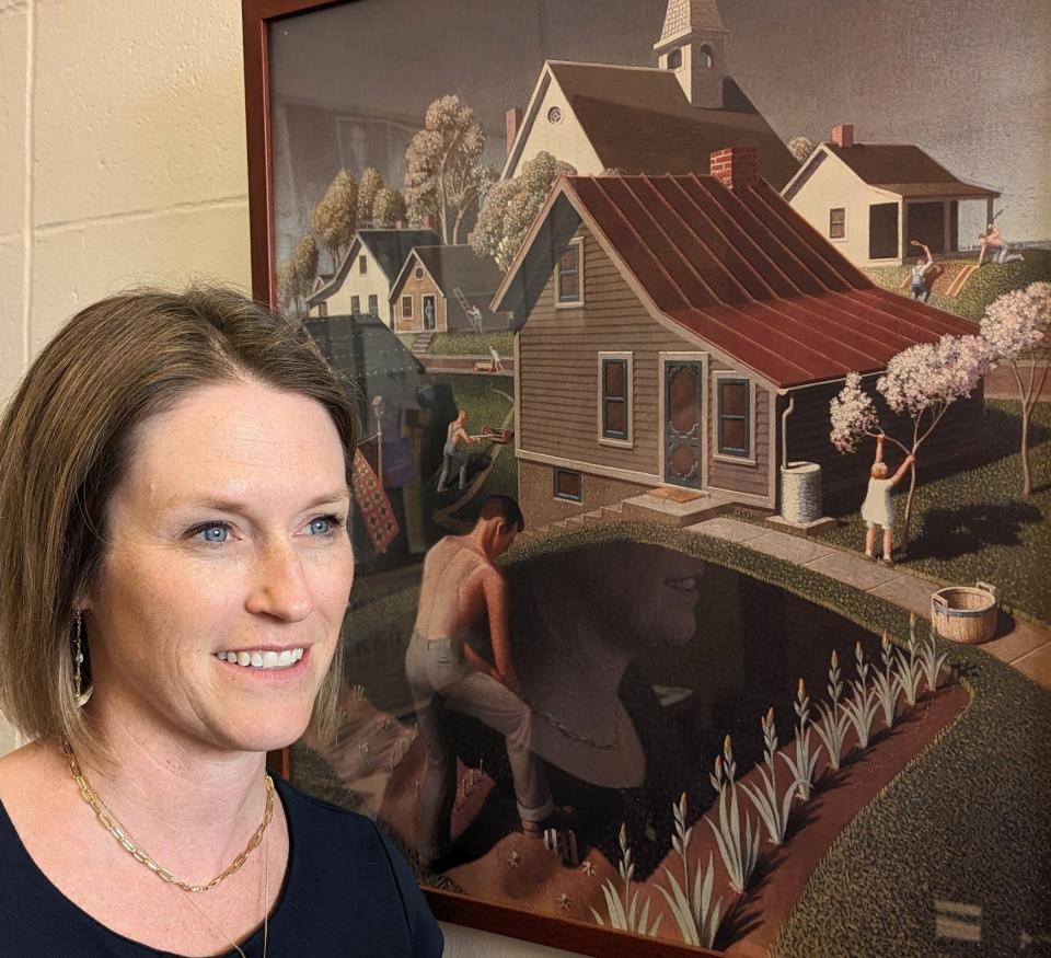 Maura Pilcher, director of the Grant Wood Art Colony, is shown in her office with a rendition of “Spring in Town” by the famed Iowa artist.