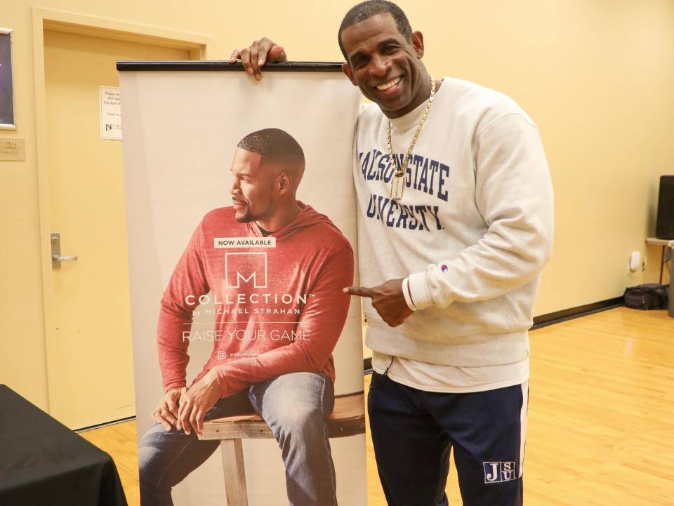 Deion Sanders points to a poster of Michael Strahan posing for Men's Wearhouse.