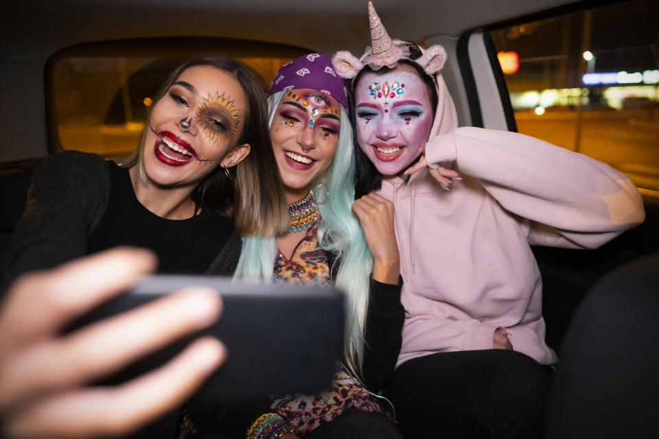 Girls riding in a taxi to the Halloween party and taking selfies.