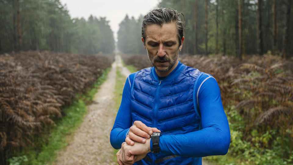 Athletic male out for a run on a rainy day in the forest. He stops to check his smartwatch for his running data