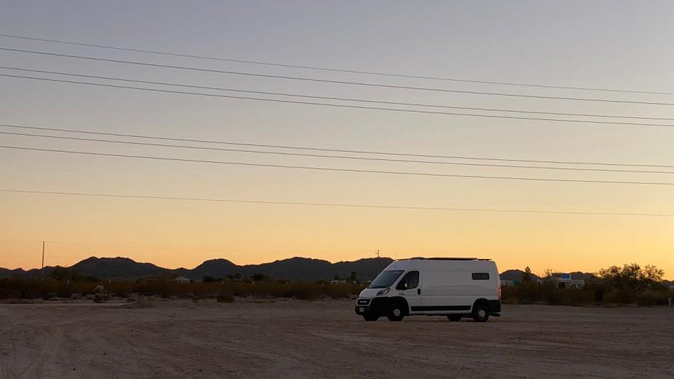 white van parked in sand in the desert with sunrise behind it