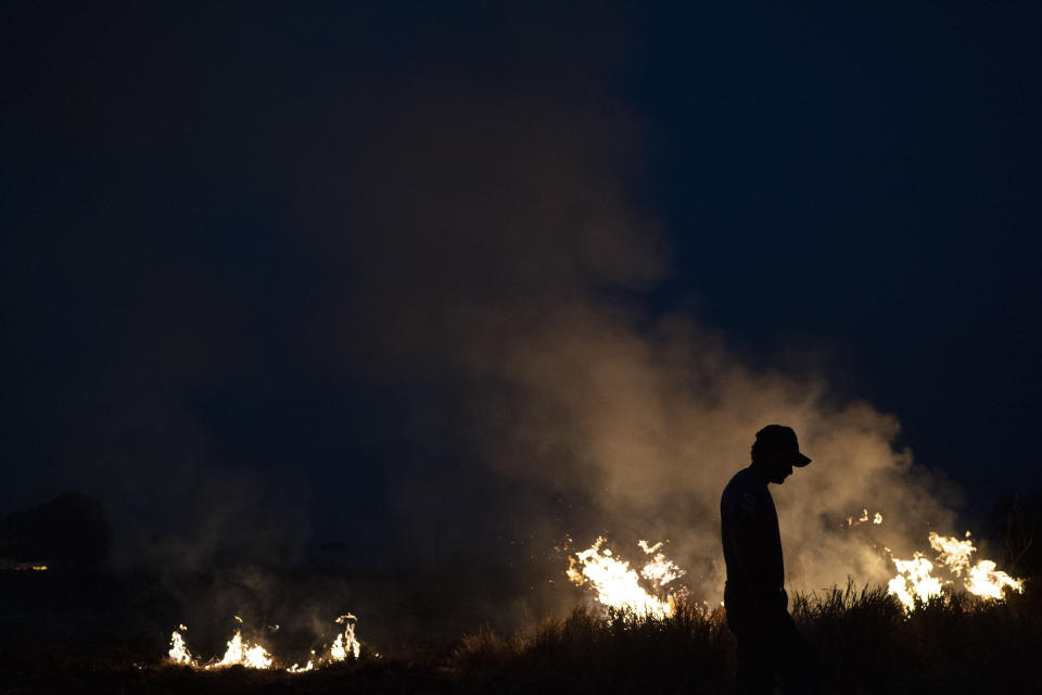 Neri dos Santos Silva, center, is silhouetted against an encroaching fire threat after he spent hours digging trenches to keep the flames from spreading to the farm he works on, in the Nova Santa Helena municipality, in the state of Mato Grosso, Brazil, Friday, Aug. 23, 2019. Under increasing international pressure to contain fires sweeping parts of the Amazon, Brazilian President Jair Bolsonaro on Friday authorized use of the military to battle the massive blazes. (AP Photo/Leo Correa)