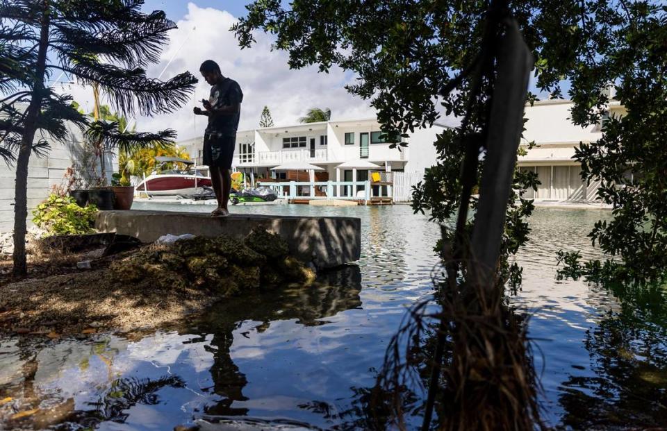 Brayan Quiñones smokes a cigarette near an overflowing canal on Monday, Oct. 30, 2023 in Miami Beach, Fla. Monday was the highest king tide of the year for South Florida, flooding streets, driveways and parks.