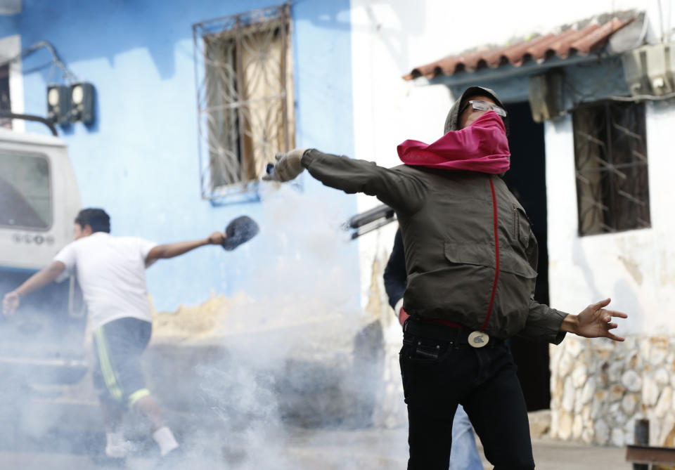 FILE In this Jan. 21, 2019 file photo, an anti-government protester throws an object at security forces as some residents show support for an apparent mutiny by a national guard unit in the Cotiza neighborhood of Caracas, Venezuela. Security forces put down the pre-dawn uprising by national guardsmen that triggered violent street protests. Socialist party chief Diosdado Cabello said at least 27 guardsmen were arrested. (AP Photo/Ariana Cubillos)