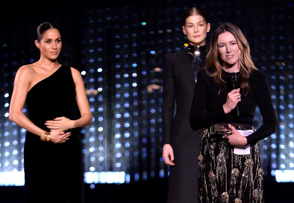 Clare Waight Keller is watched by Meghan, Duchess of Sussex and Rosamund Pike as she speaks on stage after receiving the award for British Designer of the Year Womenswear Award 