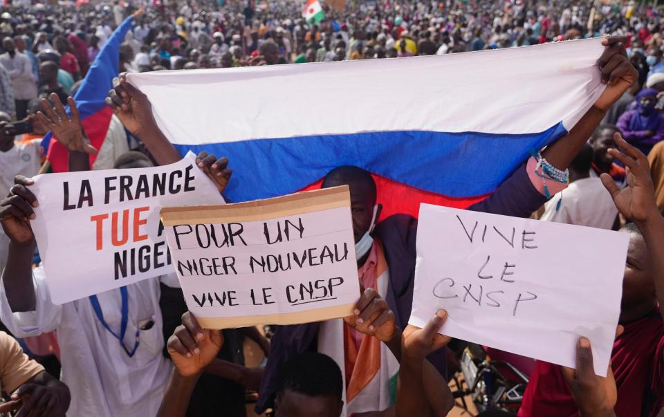 Nigeriens holding a Russian flag and placards reading ‘France kills Niger’ and ‘For a new Niger long live CNSP’