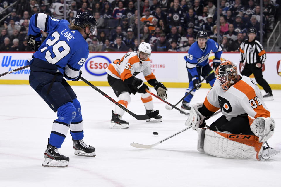 Winnipeg Jets' Patrik Laine (29) tries to pass the puck over to Mark Scheifele (55) past Philadelphia Flyers goaltender Brian Elliott (37) during second-period NHL hockey game action in Winnipeg, Manitoba, Sunday, Dec. 15, 2019. The puck deflected off Flyers' Shayne Gostisbehere (53) for a goal. (Fred Greenslade/The Canadian Press via AP)