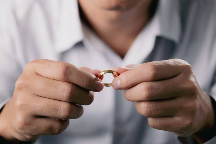 A person holding a wedding ring with both hands, partially visible face, wearing a button-down shirt