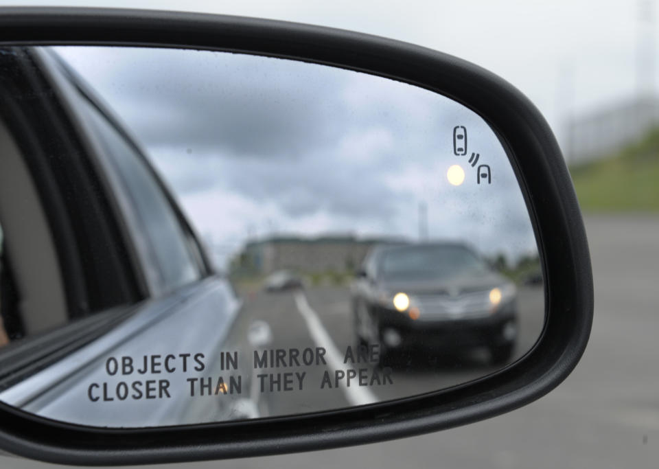 In this photo taken Tuesday, May 22, 2012, professional test driver J.D. Ellis of Cincinnati, Ohio, demonstrates the side mirror warning signal in a Ford Taurus at an automobile testing area in Oxon Hill, Md. The display at a recent transportation conference was a peek into the future of automotive safety: cars that to talk to each other and warn drivers of impending collisions. Later this summer, the government is launching a yearlong, real-world test involving nearly 3,000 cars, trucks and buses using volunteer drivers in Ann Arbor, Mich. (AP Photo/Susan Walsh)