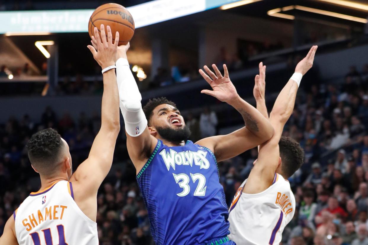 Mar 23, 2022; Minneapolis, Minnesota, USA; Minnesota Timberwolves center Karl-Anthony Towns (32) shoots between Phoenix Suns guard Landry Shamet (14) and guard Devin Booker (1) in the first quarter at Target Center.