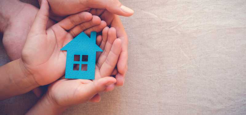 Multiple sets of hands cradle a paper house.