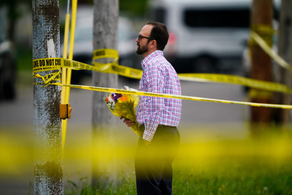 A person brings flowers to the perimeter of the scene of a shooting at a supermarket, in Buffalo, N.Y., Monday, May 16, 2022. (AP Photo/Matt Rourke)