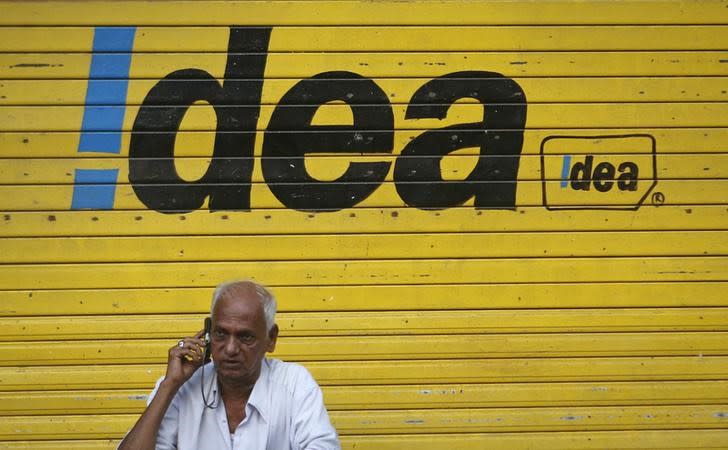 A man speaks on his mobile phone as he sits in front of a shop displaying the Idea Cellular Ltd's logo on its shutter in Mumbai April 28, 2014. REUTERS/Danish Siddiqui/Files