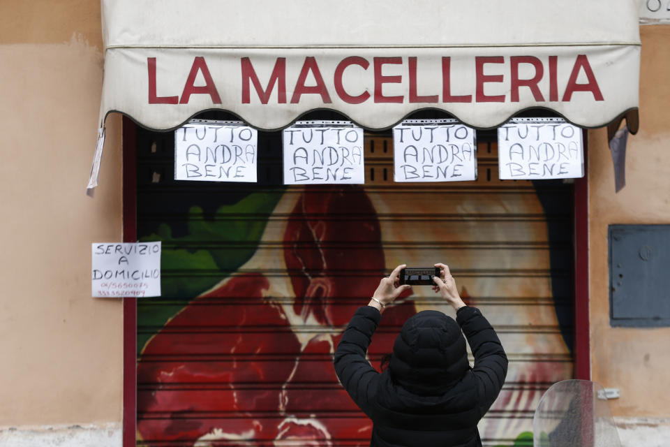 In this Friday, March 13, 2020 image, a woman take photos of notes hanging from a butchery shop and reading in Italian "Everything will be alright", in Rome Friday, March 13, 2020. The nationwide lockdown to slow coronavirus is still early days for much of Italy, but Italians are already are showing signs of solidarity. This week, children’s drawings of rainbows are appearing all over social media as well as on balconies and windows in major cities ready, ‘’Andra’ tutto bene,’’ Italian for ‘’Everything will be alright.’’ For most people, the new coronavirus causes only mild or moderate symptoms. For some, it can cause more severe illness, especially in older adults and people with existing health problems. (Cecilia Fabiano/LaPresse via AP)