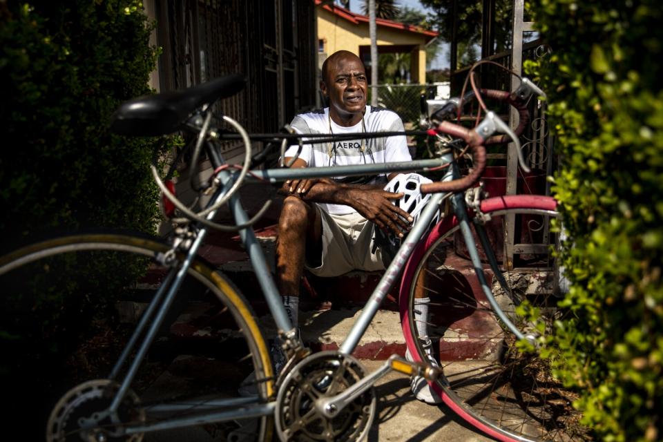 A man sits on steps behind a bicycle, with his elbows on his knees