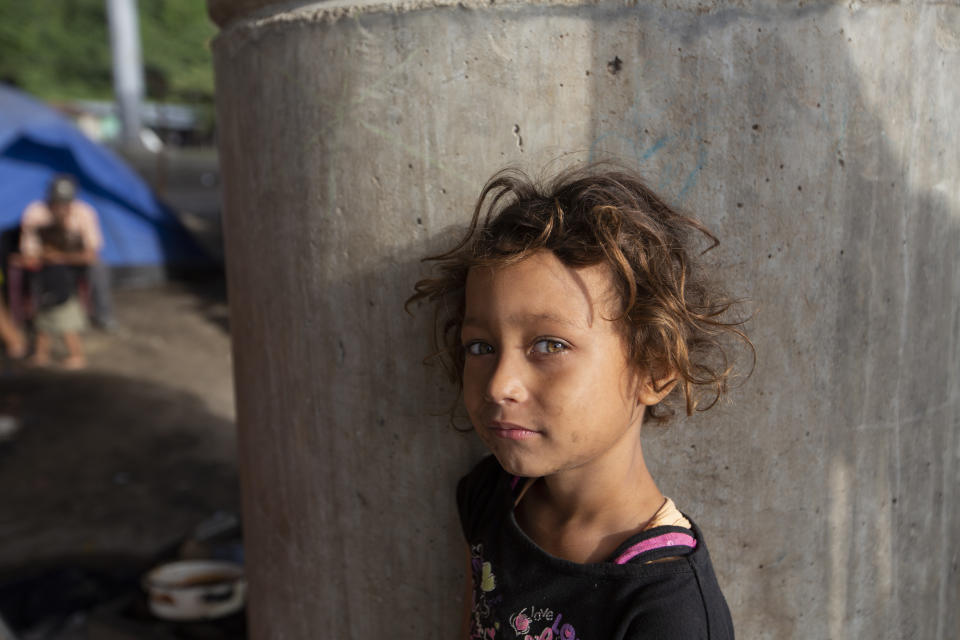 Katerine waits for breakfast cooked by her family under a bridge on the outskirts of San Pedro Sula, Honduras, Monday, Jan. 11, 2021. The 9-year-old has lived under this bridge with her family since they lost their home to last year's hurricanes Eta and Iota in November. (AP Photo/Moises Castillo)