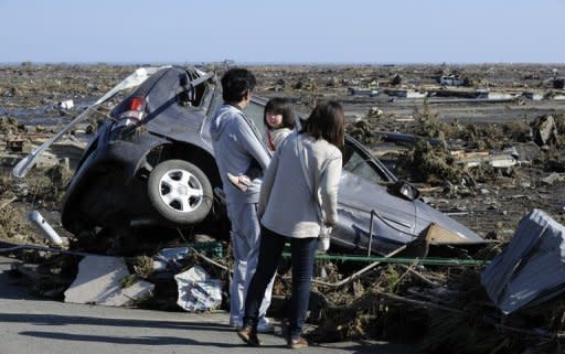 A family looks at a damaged vehicle in Minamisoma, Fukushima Prefecture
