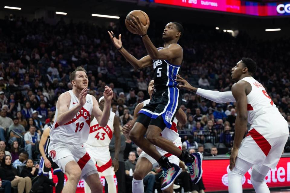 Sacramento Kings guard De’Aaron Fox (5) lays up the ball between Toronto Raptors guard RJ Barrett (9) and center Jakob Poeltl (19) during an NBA game at Golden 1 Center on Friday, Jan. 5, 2024.