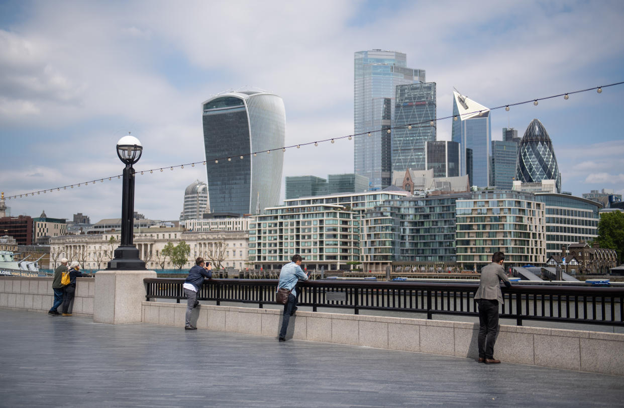 People observe social distancing as they look out at the view of the skyline of the City financial district from alongside Tower Bridge, London, following the introduction of measures to bring England out of lockdown. (Photo by Dominic Lipinski/PA Images via Getty Images)