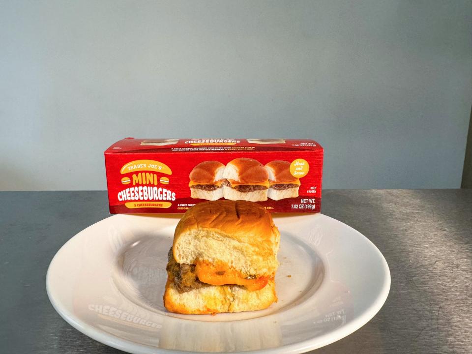 A plate with a mini cheeseburger containing oozing cheddar cheese in front of a small red box