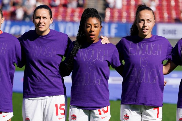 Canada’s Evelyne Viens, left, Ashley Lawrence, center and Julia Grosso line up in purple shirts bearing the slogan 'Enough is Enough' ahead of their game against Japan