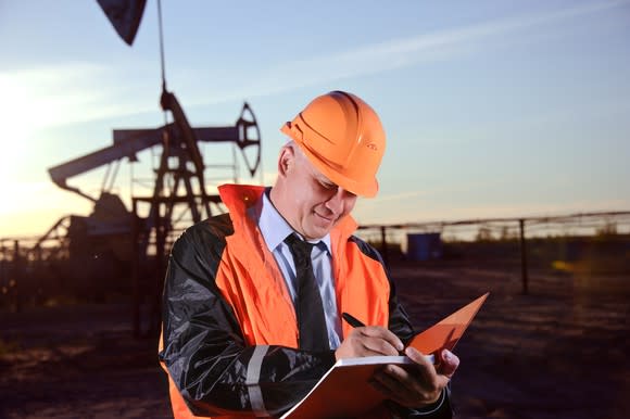 A man with a notebook in front of an oil well