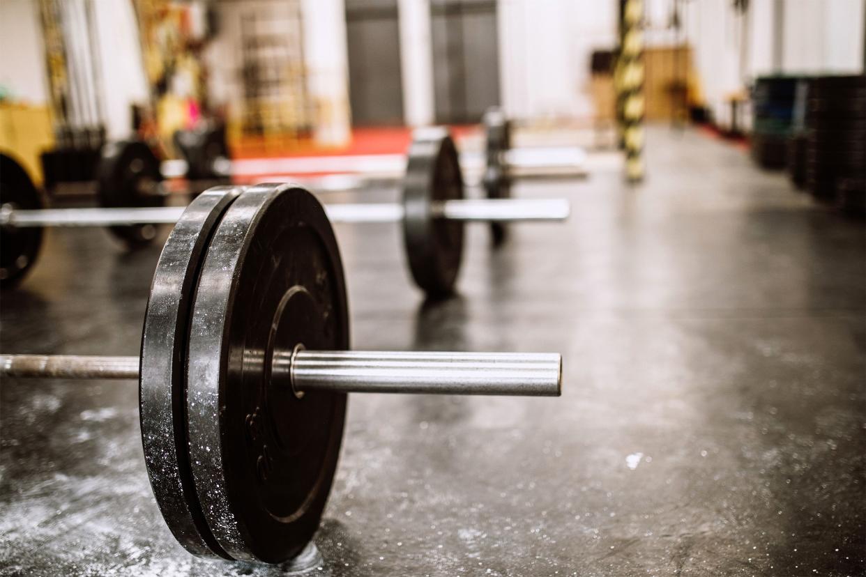 Closeup of a barbell on a black mat in an empty gym in front of a row of barbells blurred in the background