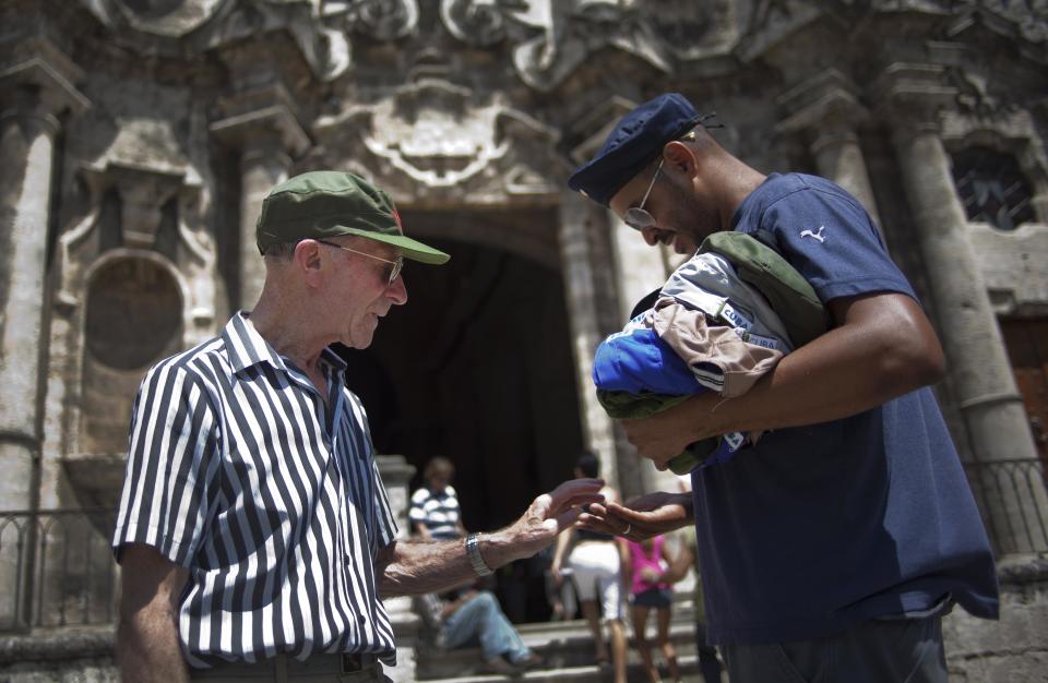 In this picture taken Sept 11, 2012, a tourist buys a baseball cap in front of the cathedral in Havana, Cuba. When the Obama administration loosened travel restrictions to Cuba, the thought was that Americans were going to pour into the island on legal cultural exchanges. But several U.S. travel operators complain that, just over a year after the U.S. re-instituted so-called people-to-people exchanges to Cuba, applications to renew their licenses are languishing, forcing cancellations, layoffs and the loss of millions of dollars in revenue. (AP Photo/Ramon Espinosa)