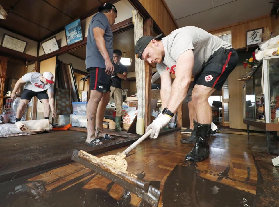 In this Oct. 13, 2019, photo, Canadian player Peter Nelson, right, volunteers to clean up mud in a house in Kamaishi, Iwate prefecture, Japan, following the cancellation of their Rugby World Cup Pool B match against Namibia due to Typhoon Hagibis. (Kyodo News via AP)