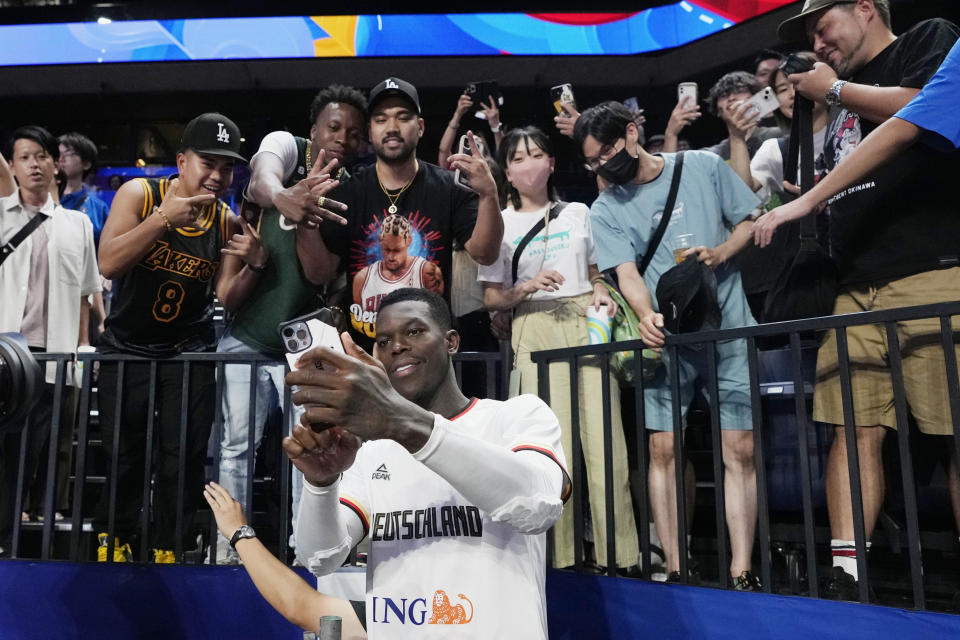 Germany guard Dennis Schroder (17) tries to make a selfie with a fan's mobile phone after the team defeated Slovenia in their Basketball World Cup group K match in Okinawa, southern Japan, Sunday, Sept. 3, 2023. (AP Photo/Hiro Komae)