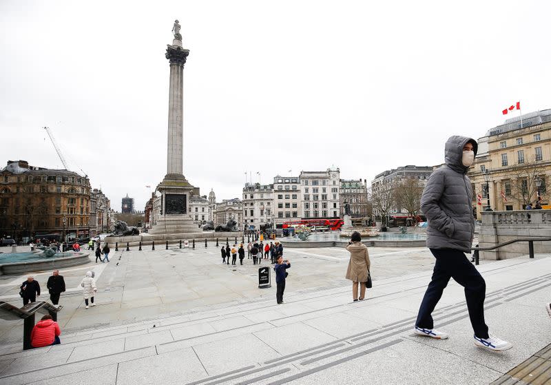 A man wearing a protective face mask walks through Trafalgar Square, as the number of coronavirus cases grow around around the world, in London