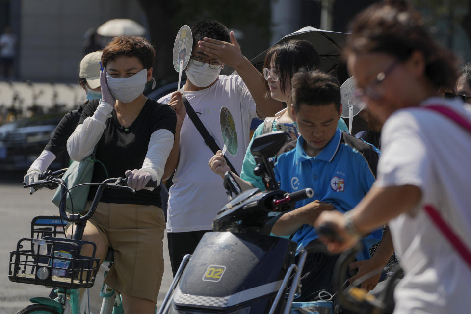 A boy holding a fan wipes his sweat as people wait to cross a traffic intersection on a sweltering day in Beijing, Monday, July 10, 2023. Rescuers were looking Monday for several people missing in a landslide triggered by torrential rains while employers across much of China were ordered to limit outdoor work due to scorching temperatures as the country struggled with heat, flooding and drought. (AP Photo/Andy Wong)