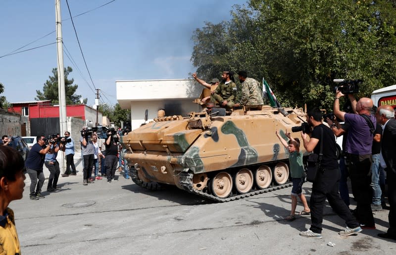 Turkey-backed Syrian rebel fighters on an armoured personnel carrier react as they drive to cross into Syrian town of Tal Abyad