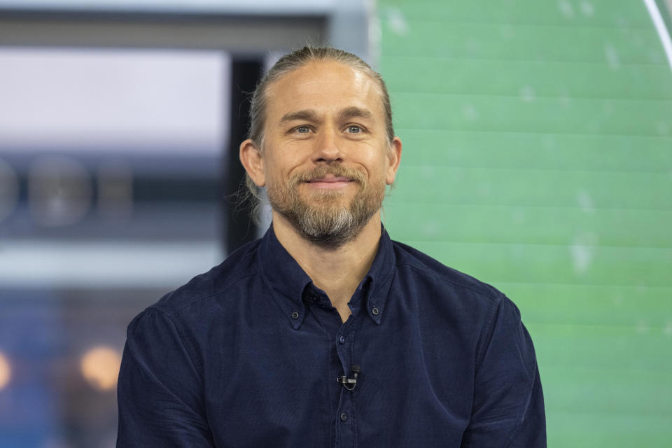 Charlie Hunnam smiling, wearing a button-down shirt, and sporting a neatly pulled-back ponytail